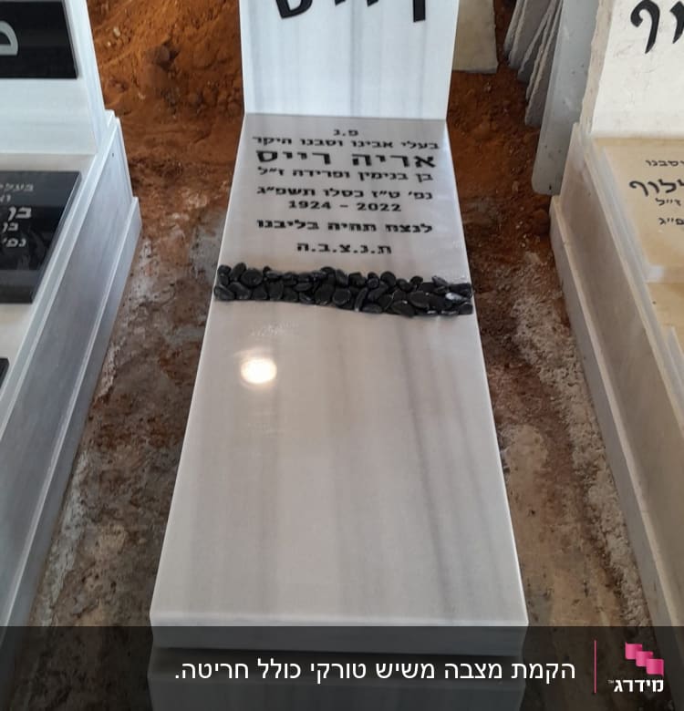 מצבה לבנה עם כיתוב בעברית ואבנים שחורות